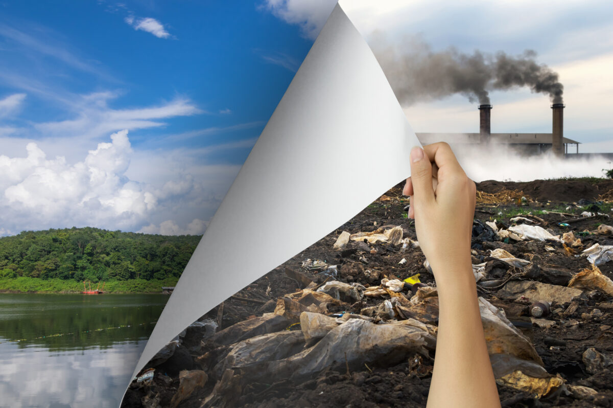 Hand revealing a clean natural landscape behind a polluted industrial scene with smoke and garbage, symbolizing the transition from pollution to sustainability.