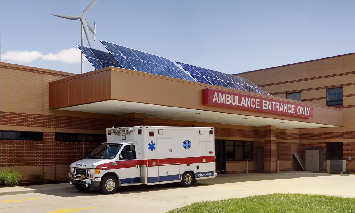 Krankenhausgebäude mit installierten Solarpaneelen und Windturbine, Symbol für Mikronetzlösungen zur Versorgung kritischer Infrastrukturen.