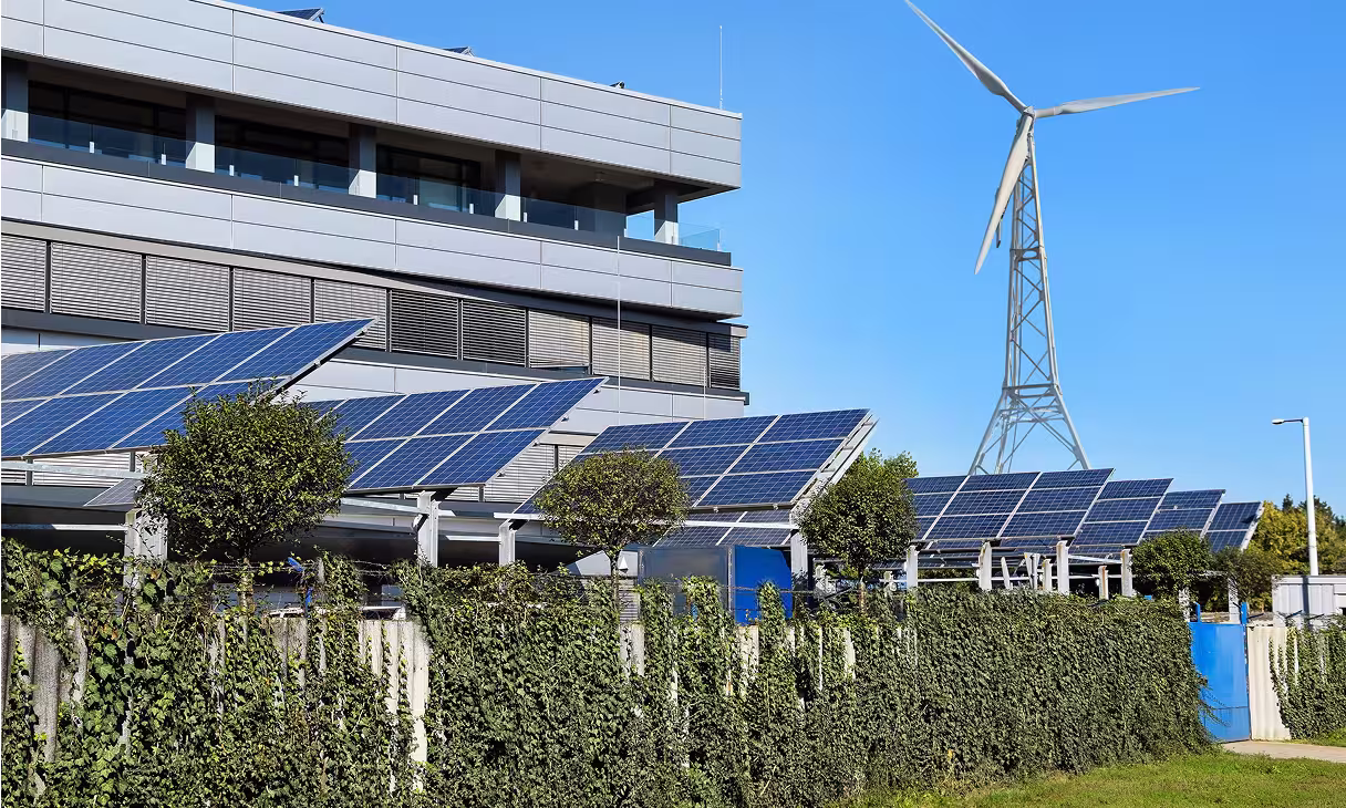 Büro- oder Industriegebäude mit Solarpaneelen und Windturbine, die nachhaltige Energieversorgung für Unternehmen veranschaulichen.