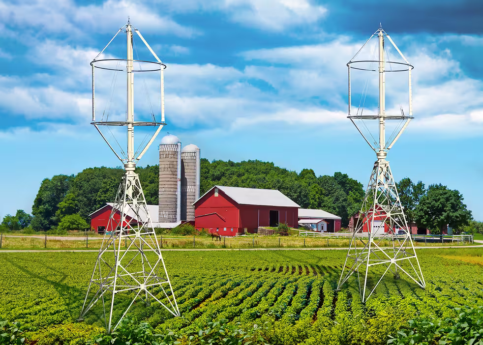 Zwei vertikale Windturbinen auf Ackerland neben roten Scheunen – Symbol für die Integration erneuerbarer Energien in der Landwirtschaft.