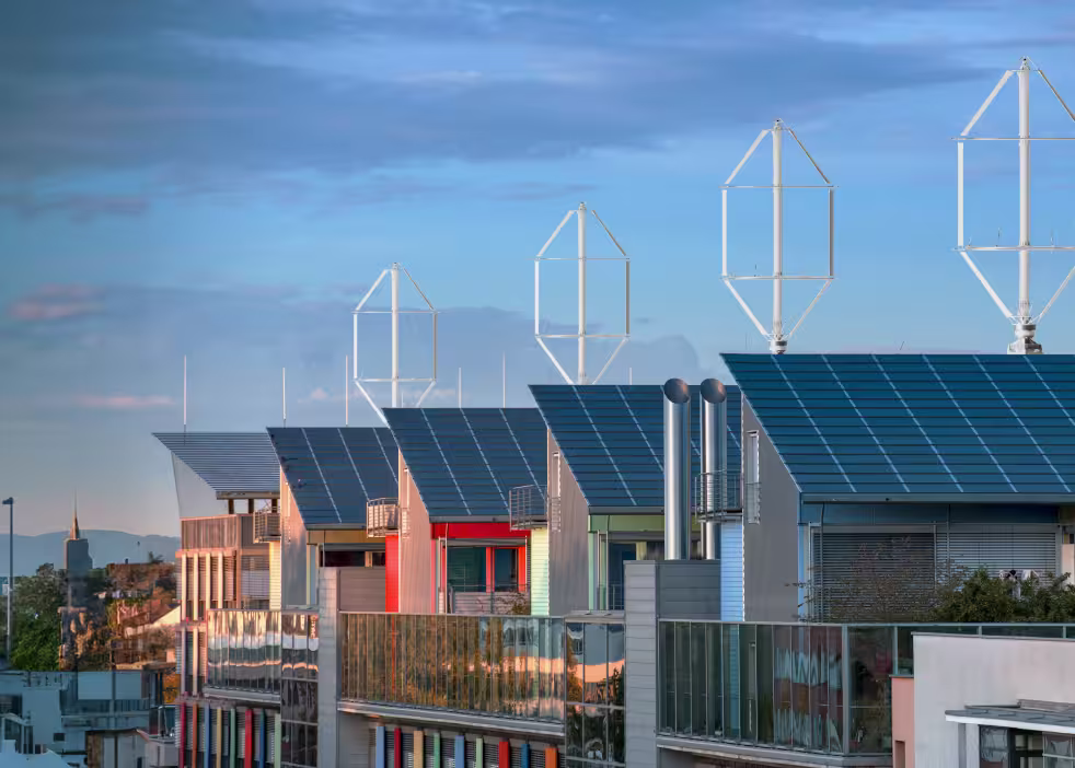 Moderne Wohngebäude mit Solarmodulen und vertikalen Windturbinen auf den Dächern – ein Beispiel für die Integration erneuerbarer Energien in städtische Gebiete.